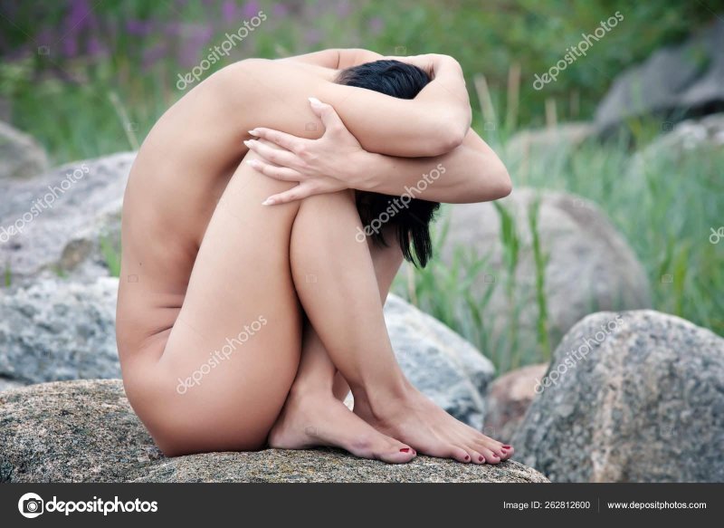 Naked woman sits on a stone